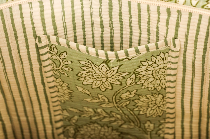 Pu&ograve; includere: Primo piano dell'interno di una borsa tote. La fodera presenta strisce verticali color crema e verdi. &Egrave; visibile una tasca, che mostra un motivo floreale in verde e bianco. Il design della borsa suggerisce un'estetica naturale.