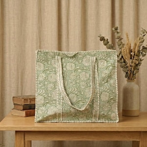 Pu&ograve; includere: Una borsa tote verde con un motivo floreale e finiture bianche &egrave; appoggiata su un tavolo di legno. La borsa ha due manici ed &egrave; accanto a una pila di libri e un vaso con piante essiccate.
