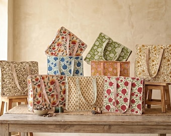 Op de afbeelding: Een verzameling tote bags met patronen in verschillende kleuren, waaronder bloemen- en fruitontwerpen. De tassen worden tentoongesteld op een houten tafel en krukken, waarbij hun verschillende patronen en stijlen worden getoond. De tassen hebben bijpassende handvatten.