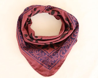 Könnte beinhalten: Ein weinrotes Bandana mit Paisley- und Blumenmuster in Dunkelblau und Schwarz. Das quadratische Tuch ist gefaltet und geknotet, wodurch eine kreisförmige Form entsteht. Der Stoff wirkt weich und leicht.