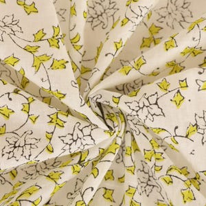 May include: Cream-colored fabric with a repeating pattern of black floral outlines and bright yellow leaves. The fabric is folded and gathered, showing the detailed design. Ideal for sewing projects or home decor.