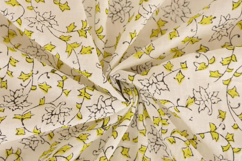 May include: Cream-colored fabric with a repeating pattern of black floral outlines and bright yellow leaves. The fabric is folded and gathered, showing the detailed design. Ideal for sewing projects or home decor.