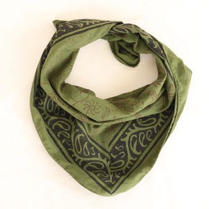 Op de afbeelding: Olijfgroene bandana met een zwart paisley- en bloemenpatroon. De vierkante sjaal is in een driehoek gevouwen. De stof heeft een zachte, licht gekreukelde textuur. De bandana wordt op een witte achtergrond weergegeven.