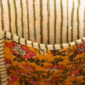 Op de afbeelding: Close-up van een stoffen interieur met een zak. Het interieur heeft verticale strepen in wit en olijfgroen. De zak is mosterdgeel met een bloemenpatroon in roze en wit.