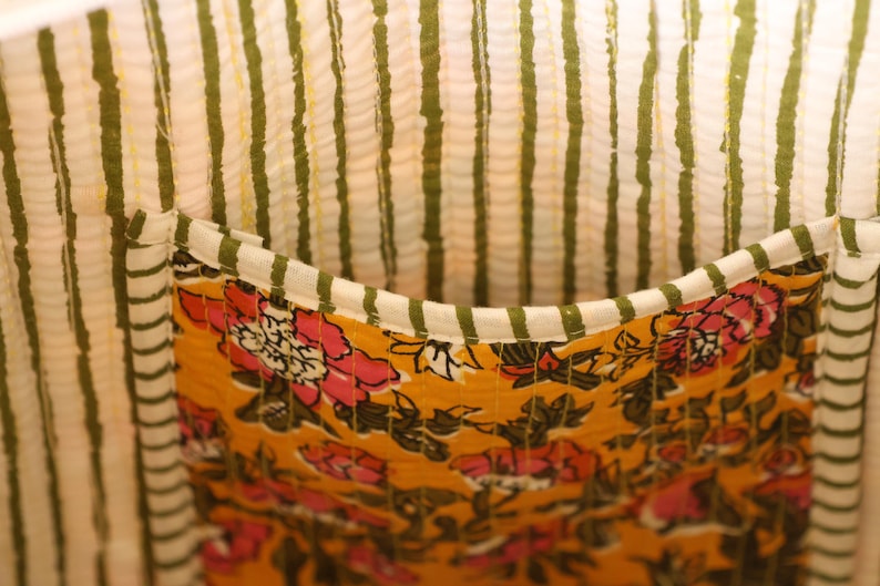 Op de afbeelding: Close-up van een stoffen interieur met een zak. Het interieur heeft verticale strepen in wit en olijfgroen. De zak is mosterdgeel met een bloemenpatroon in roze en wit.