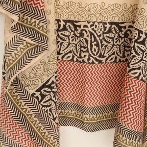 May include: A beige textile with a repeating pattern of black, red, and olive green geometric and floral designs. The fabric features a variety of patterns, including zigzags, paisley, and leaf motifs, creating a layered and textured appearance.