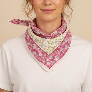 Puede incluir: Un pañuelo con estampado floral rosa y blanco se lleva alrededor del cuello. El pañuelo tiene forma cuadrada y está hecho de una tela suave. Es un accesorio de moda que se lleva con una camiseta blanca.