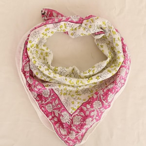 May include: A square scarf with a floral pattern. The scarf features a white background with a repeating pattern of yellow and green leaves. The border is a vibrant pink with a floral design. The scarf is folded and tied.