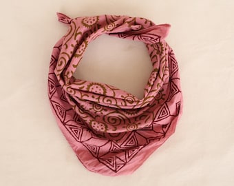 Könnte beinhalten: Ein rosa Bandana mit einem braunen geometrischen und floralen Muster. Das Bandana ist oben gefaltet und gebunden, mit einer dreieckigen Form unten. Der Stoff hat ein weiches, leicht zerknittertes Aussehen.