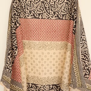 May include: A patterned textile with a variety of designs. The fabric features alternating bands of black floral patterns, red zigzags, and a cream-colored section with small circular motifs. The edges have a geometric border.