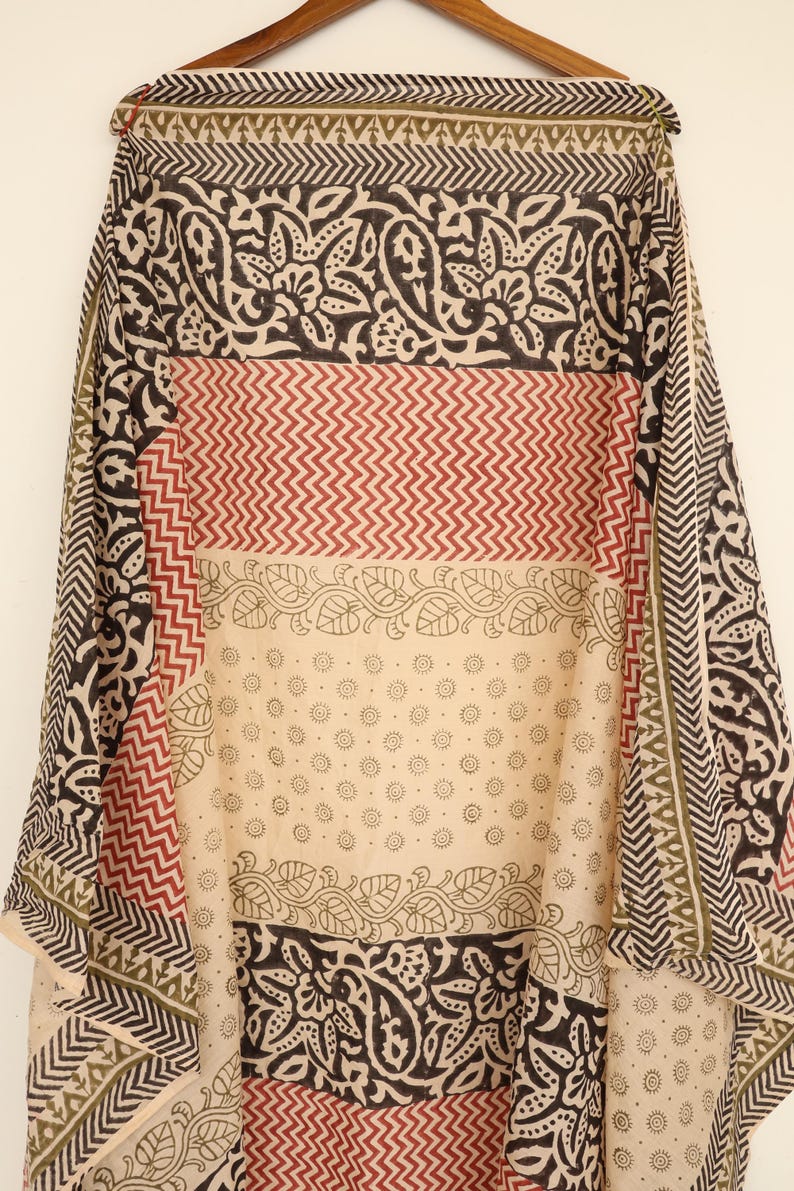 May include: A patterned textile with a variety of designs. The fabric features alternating bands of black floral patterns, red zigzags, and a cream-colored section with small circular motifs. The edges have a geometric border.