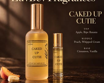 May include: A large frosted glass perfume bottle and a smaller rollerball bottle labeled LuvBev Fragrances Caked Up Cutie. The text lists scent notes including apple, ripe banana, peach, whipped cream, cinnamon, and vanilla. A peach slice and banana slice sit nearby.