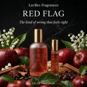 May include: Two glass perfume bottles with gold caps are displayed. The larger bottle and smaller rollerball bottle are filled with a red liquid. The bottles are labeled "RED FLAG" and surrounded by red apples, cinnamon sticks, and white flowers.