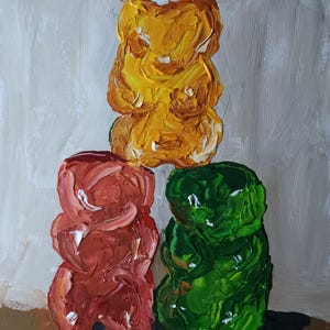 Könnte beinhalten: Ein originales Ölgemälde von drei Gummibärchen. Das Gemälde zeigt ein gelbes Gummibärchen, das auf einem roten und grünen Gummibärchen gestapelt ist. Das Gemälde hat einen strukturierten, pastosen Stil mit sichtbaren Pinselstrichen.