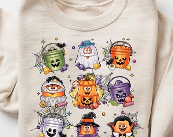 May include: Beige sweatshirt featuring a colorful Halloween-themed graphic. The graphic includes various cartoon characters such as pumpkins, ghosts, and vampires. The design is surrounded by spiderwebs, creating a festive and playful look.