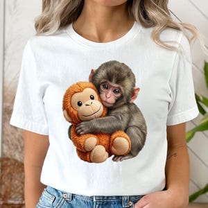 May include: White t-shirt featuring a graphic of two monkeys hugging. One monkey is brown and the other is orange. The shirt is made of a soft, comfortable material.