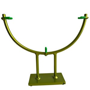 May include: A gold-colored metal stand with a curved top and a rectangular base. The stand has two vertical supports and a central support, with green accents at the top. The stand is designed to hold an item.