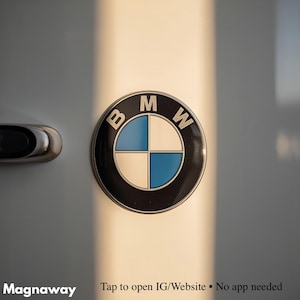 May include: A close-up of a BMW emblem, featuring a black outer ring with the letters "B", "M", and "W". The emblem's center is divided into four quadrants: two white and two blue. The emblem is affixed to a light-colored surface.