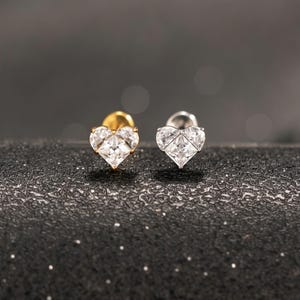 May include: Two stud earrings shaped like hearts, each featuring a clear, faceted gemstone. One earring is set in a gold-toned metal, while the other is set in a silver-toned metal. Both earrings have a pointed base and a rounded top edge.