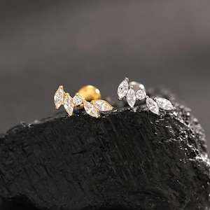 May include: Two stud earrings featuring a leaf-like arrangement of clear marquise and round-cut stones. One earring is set in a gold-toned metal, while the other is set in a silver-toned metal, both showcasing a cluster of sparkling faceted gems.