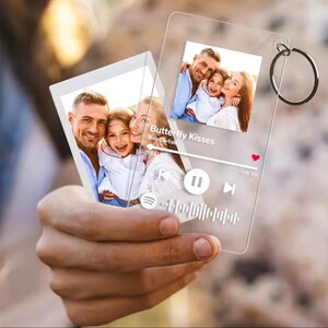 May include: Clear acrylic keychain featuring a family photo and a music player interface. The text "Butterfly Kisses" is visible. The keychain includes a silver metal ring for attachment.