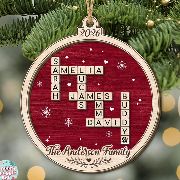 Puede incluir: Un adorno navideño redondo de madera con un fondo rojo intenso que presenta una cuadrícula de crucigrama con los nombres Sarah, Amelia, Lucas, James, Emma, David y Buddy. El texto 2026 y The Anderson Family están grabados en la madera.