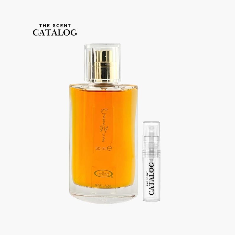 May include: A perfume bottle with a gold cap and a clear glass body filled with amber liquid. A smaller sample bottle is next to it. The text "THE SCENT CATALOG" is at the top, and the main bottle has "50 ml e" printed on it.