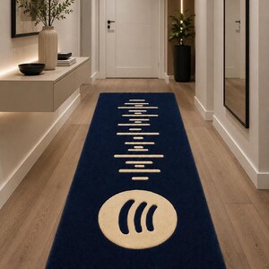 Könnte beinhalten: Ein rechteckiger Läufer in tiefem Marineblau mit einem cremefarbenen Grafikdesign. Das Muster zeigt ein vertikales Schallwellenmotiv über einem kreisförmigen Symbol mit drei geschwungenen Linien. Der Text CozyArtisanRugs ist zu sehen.