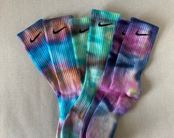 May include: Five pairs of colorful tie-dye socks with black Nike logos. The socks are in shades of blue, green, and purple.
