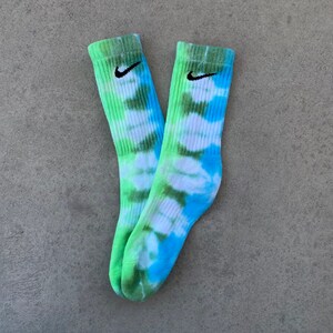 May include: A pair of green, blue, and white tie-dye socks with a black Nike swoosh logo on each sock.