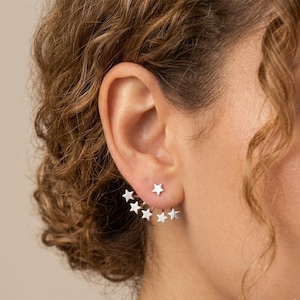 May include: Silver star earrings. One earring has a single star, the other has a series of graduated stars. The earrings are worn on the earlobe and curve up the ear. The earrings are a simple, elegant design.