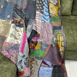 May include: A patchwork quilt draped over a green sofa. The quilt features a variety of fabric patterns and colors, including blue, pink, brown, and green. The stitching is visible, adding to the handmade aesthetic. The quilt is a decorative textile.