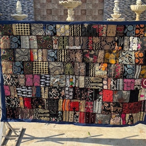 Puede incluir: Un textil de patchwork con un borde azul oscuro. El textil está compuesto por numerosos parches rectangulares en varios colores y patrones, incluyendo diseños florales y geométricos. El texto "PrintBell" es visible.