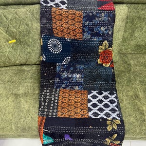 Pode incluir: Um edredom de retalhos com uma variedade de padr&otilde;es e cores. O edredom apresenta quadrados de tecido preto, azul marinho, laranja e branco. Alguns quadrados t&ecirc;m desenhos florais, outros padr&otilde;es geom&eacute;tricos. O edredom est&aacute; em um sof&aacute; verde.