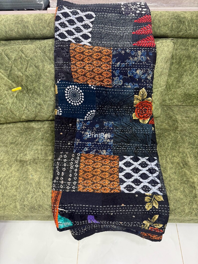 Pode incluir: Um edredom de retalhos com uma variedade de padr&otilde;es e cores. O edredom apresenta quadrados de tecido preto, azul marinho, laranja e branco. Alguns quadrados t&ecirc;m desenhos florais, outros padr&otilde;es geom&eacute;tricos. O edredom est&aacute; em um sof&aacute; verde.
