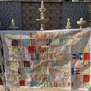 May include: A patchwork quilt with a white border, displayed outdoors. The quilt is composed of numerous rectangular fabric pieces in various colors and patterns, including floral, paisley, and geometric designs. The overall aesthetic is rustic and handcrafted.