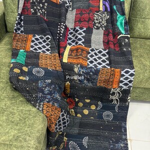 Pode incluir: Uma colcha de retalhos com uma variedade de quadrados de tecido estampado em tons de preto, castanho, vermelho e branco. A colcha est&aacute; sobre um sof&aacute; verde, mostrando seu design intrincado e texturas. A costura da colcha &eacute; vis&iacute;vel.