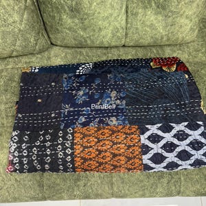 Pode incluir: Um t&ecirc;xtil de patchwork com uma variedade de padr&otilde;es e cores, incluindo desenhos florais, geom&eacute;tricos e abstratos. O t&ecirc;xtil &eacute; feito de diferentes quadrados de tecido costurados com fio branco. A paleta de cores inclui azul marinho, laranja e branco.