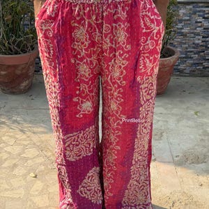 May include: Red, loose-fitting trousers with an elasticated waist and a gold and purple floral design. The trousers have pockets and are made of a soft fabric. The text "PrintBell" is visible on the trousers.