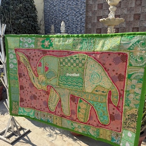 May include: A decorative textile featuring an elephant design. The elephant is primarily green with gold accents, set against a pink background. The border is green with various embroidered patterns. The text "PrintBell" is visible.