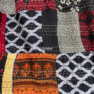 Pode incluir: Close-up de um tecido patchwork com v&aacute;rios padr&otilde;es e cores. O design inclui formas geom&eacute;tricas, motivos paisley e florais em vermelho, preto, branco, laranja e azul. O tecido &eacute; costurado com fio branco.