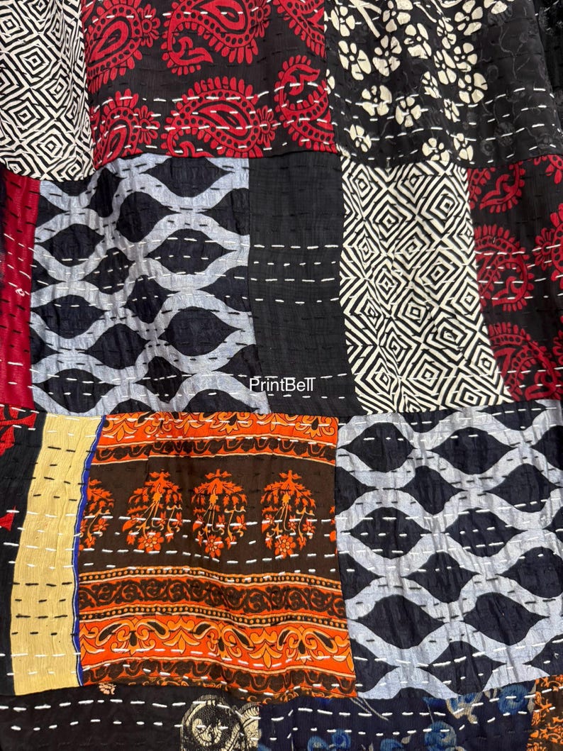 Pode incluir: Close-up de um tecido patchwork com v&aacute;rios padr&otilde;es e cores. O design inclui formas geom&eacute;tricas, motivos paisley e florais em vermelho, preto, branco, laranja e azul. O tecido &eacute; costurado com fio branco.