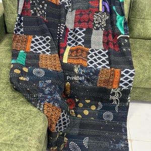 Pode incluir: Um edredom de retalhos com uma variedade de quadrados de tecido estampado em tons de preto, laranja, vermelho e branco. O edredom &eacute; drapeado sobre um sof&aacute; verde, mostrando seu design intrincado e texturas. O edredom tem o texto "PrintBell".