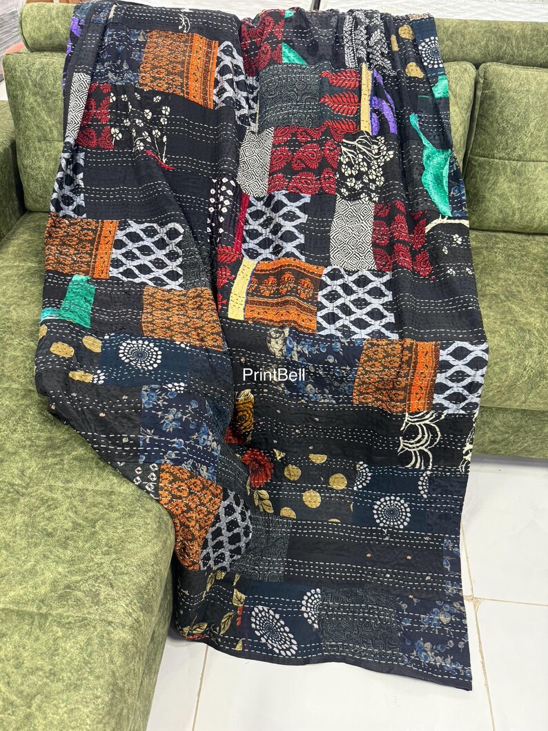 Pode incluir: Um edredom de retalhos com uma variedade de quadrados de tecido estampado em tons de preto, laranja, vermelho e branco. O edredom &eacute; drapeado sobre um sof&aacute; verde, mostrando seu design intrincado e texturas. O edredom tem o texto "PrintBell".