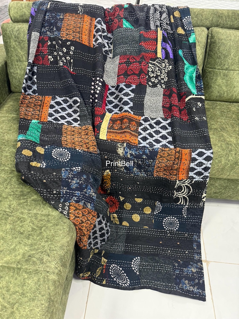 Pode incluir: Um edredom de retalhos com uma variedade de quadrados de tecido estampado em tons de preto, laranja, vermelho, branco e azul. O edredom est&aacute; sobre um sof&aacute; verde, mostrando seu design e texturas intrincados.