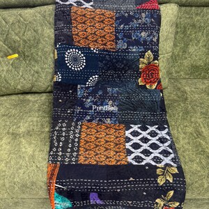Pode incluir: Um edredom de retalhos com uma variedade de quadrados estampados em tons de preto, azul marinho, laranja e branco. O edredom apresenta desenhos florais e geom&eacute;tricos, com costuras vis&iacute;veis. O edredom est&aacute; sobre um sof&aacute; verde.