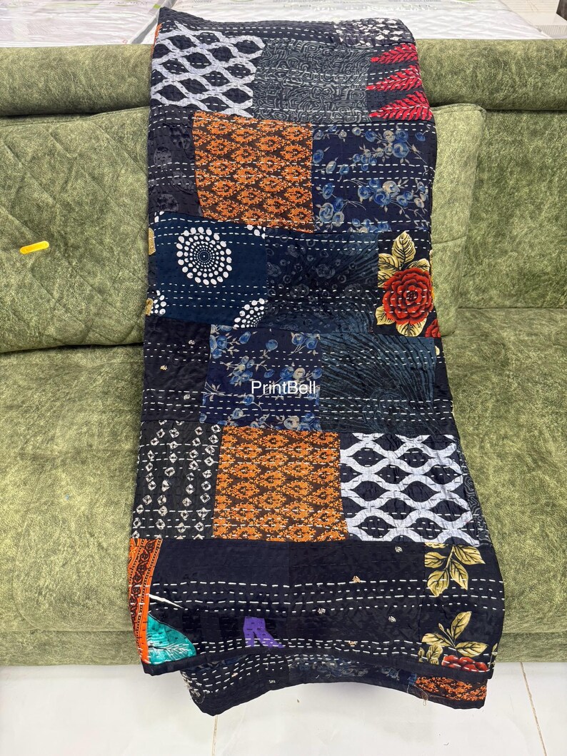Pode incluir: Um edredom de retalhos com uma variedade de quadrados estampados em tons de preto, azul marinho, laranja e branco. O edredom apresenta desenhos florais e geom&eacute;tricos, com costuras vis&iacute;veis. O edredom est&aacute; sobre um sof&aacute; verde.