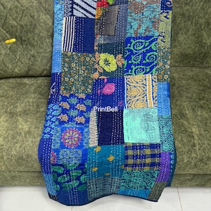 May include: A rectangular patchwork quilt featuring a variety of blue, green, and yellow fabric squares with diverse floral, geometric, and abstract patterns. The textile is stitched with visible white running thread and displays the text Printbell.