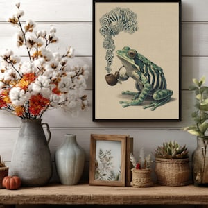 Könnte beinhalten: Ein gerahmter Kunstdruck mit einem grünen Frosch, der eine Pfeife raucht, mit einem wirbelnden Rauchdesign. Der Frosch hat grüne und schwarze Streifen. Das Kunstwerk wird auf einem Holzregal mit Vasen, einem kleinen Kürbis und anderen dekorativen Gegenständen ausgestellt.