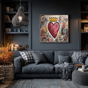 May include: A framed artwork featuring a large pink heart with a gold crown, surrounded by colorful graffiti-style drawings. The artwork hangs above a gray sofa with pillows and a blanket, in a room with a dark blue wall and a woven pendant light.